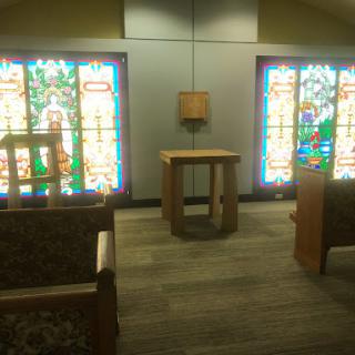 A serene interior space featuring stained glass windows and simple wooden furniture.