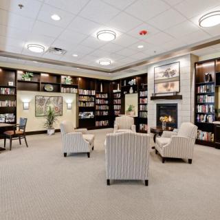 A cozy library room featuring armchairs, a fireplace, and bookshelves filled with books.