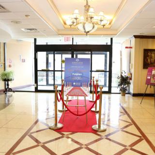 A hotel lobby featuring a red carpet and roped-off entrance with signage, illuminated by chandeliers.
