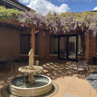 A serene courtyard featuring a charming fountain and lush wisteria in bloom.