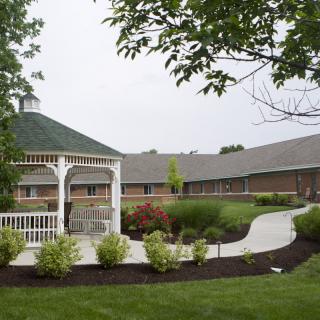 A scenic view of a gazebo and pathway surrounded by lush gardens and a building in the background.