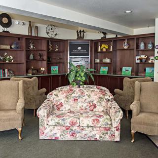 A cozy living room with a floral couch and armchairs, surrounded by wooden bookshelves and decor.