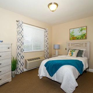 A cozy bedroom with a neatly made bed, a lamp on the bedside table, and a dresser near the window.