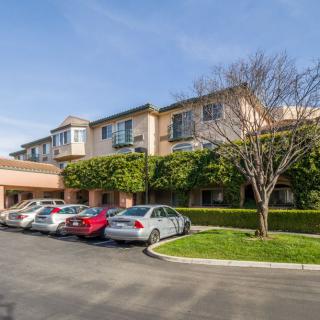 A sunny day view of a building with cars parked in the driveway.