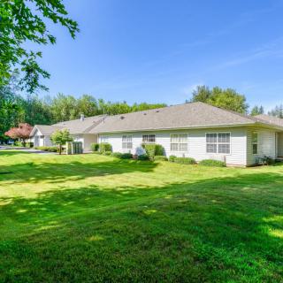 A single-story residential house with a well-maintained lawn and surrounding trees under a clear blue sky.