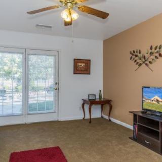 A cozy living room featuring a ceiling fan, television, decorative wall art, and glass doors leading to the outside.