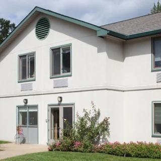 A two-story residential building with white walls and a green roof.