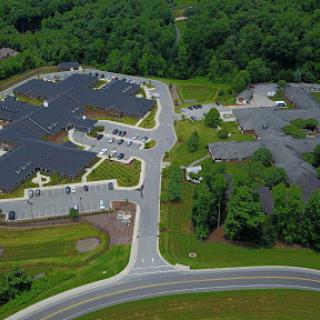 An aerial view showcasing a complex with solar panel installations, surrounded by lush greenery and organized parking areas.