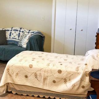 A cozy bedroom featuring a bed with a patterned blanket and a small sofa beside it.