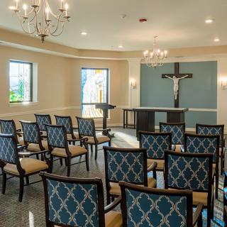 A small chapel interior with rows of chairs facing an altar and a crucifix.