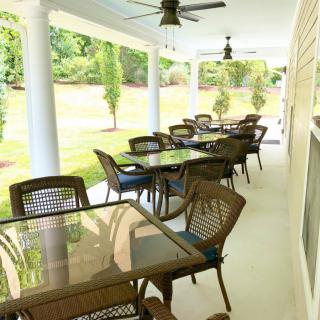 A covered patio area with several tables and chairs, overlooking a garden.
