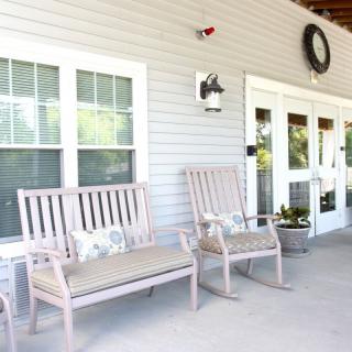 A cozy porch with benches and rocking chairs, complemented by a decorative wreath and wall-mounted light.