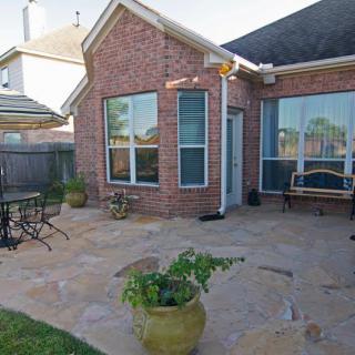 A cozy backyard patio with seating, potted plants, and a brick house.