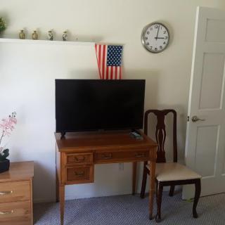 A living room setup featuring a television on a wooden desk, an American flag, and a wall clock.