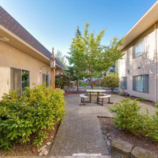 A peaceful courtyard with a central seating area surrounded by plants and buildings under a clear blue sky.
