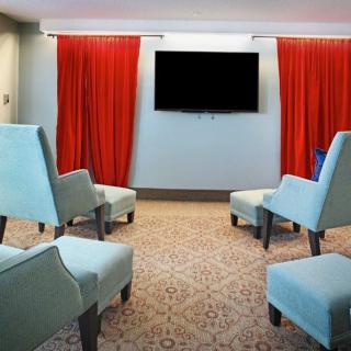 A cozy living room with pastel chairs and red curtains focused around a mounted television.