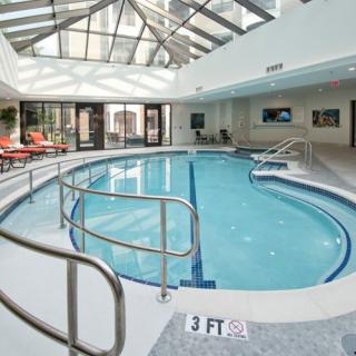 A serene indoor swimming pool with a glass ceiling and relaxation chairs.