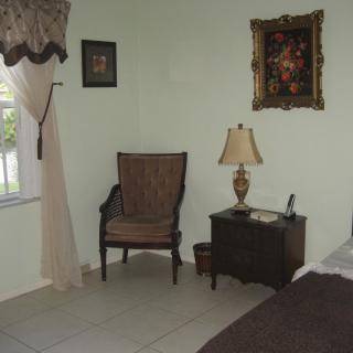 A cozy bedroom corner featuring a wooden chair, a nightstand with a lamp, and wall art.