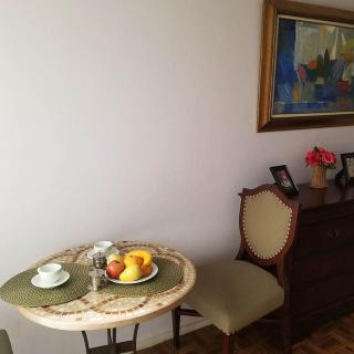 A cozy dining area featuring a small round table set with a fruit bowl and teacup, flanked by cushioned chairs and adorned with artwork on the wall.