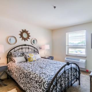 A cozy bedroom with a metal bed frame and patterned bedding, featuring decorative mirrors and bedside lamps.