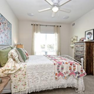 A cozy bedroom with a quilt-covered bed, decorative pillows, and a ceiling fan.