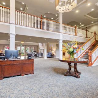 A spacious and elegant lobby featuring a wooden desk, a grand staircase, and a chandelier.