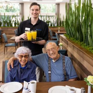 A cheerful elderly couple enjoying drinks with a friendly waiter at a restaurant.