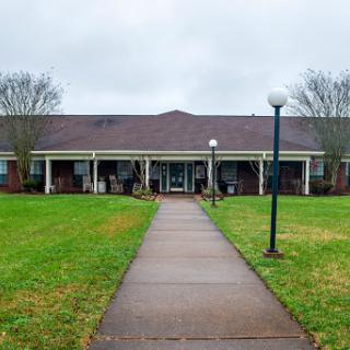 A view of a residential building with a pathway leading to the entrance, surrounded by grass under a cloudy sky.