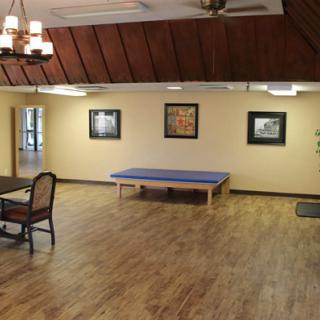 A spacious interior room featuring a table, chairs, artwork on the walls, and hardwood flooring.