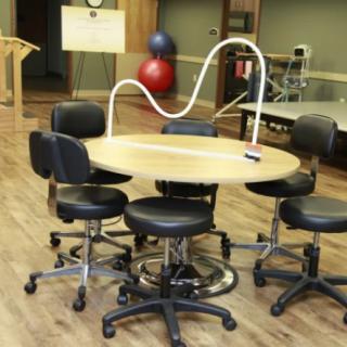 A therapy room with a round table surrounded by chairs and exercise equipment.