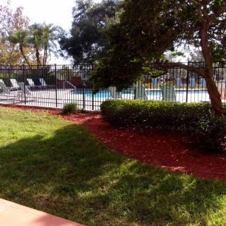 A fenced swimming pool area with lounge chairs, surrounded by greenery and landscaping.