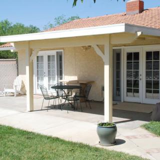 A cozy patio area with a table and chairs under an awning, set against a house with glass doors leading to a backyard.