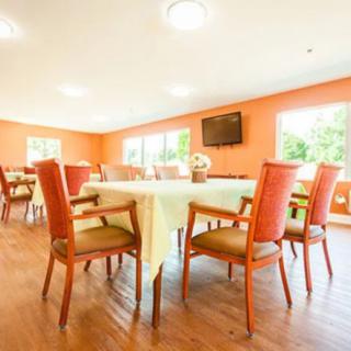A brightly lit dining area with orange walls, wooden floors, and arranged tables and chairs.