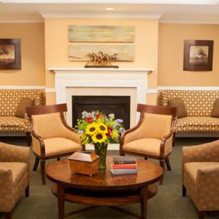 A cozy living room with comfortable chairs arranged around a central table and a fireplace, decorated with vibrant sunflowers.
