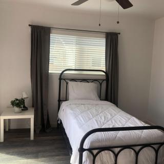 A minimalist bedroom with a single metal-framed bed and a nightstand by the window, accented by dark curtains.