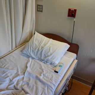 An empty hospital bed in a patient room with white sheets and medical equipment.