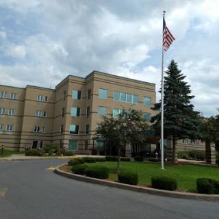 A view of a modern building with an American flag in front, surrounded by greenery.