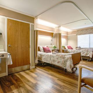 A spacious and well-lit patient room in a hospital, featuring two beds and modern furnishings.