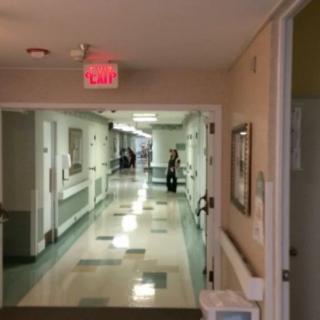 A quiet hospital corridor with an exit sign and medical equipment along the walls.