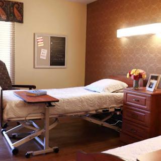 A serene hospital patient room featuring a neatly made bed, a comfortable chair, and personal touches on the nightstand.