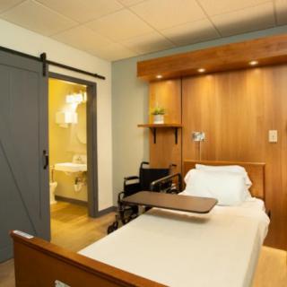 A modern hospital room featuring a patient bed and wheelchair, with an adjoining bathroom.