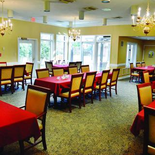A spacious dining room with neatly arranged tables and red tablecloths, illuminated by elegant chandeliers.