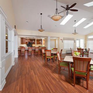 A spacious dining area with hardwood flooring, featuring tables and chairs, ceiling fans, and abundant natural light.
