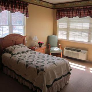 A cozy bedroom with a single bed, a chair by the window, and a small nightstand.