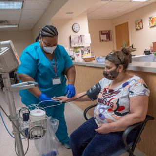 A nurse assists a patient with a blood pressure monitor in a clinic setting.