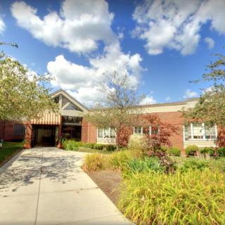 A school building with a landscaped entrance, under a partly cloudy sky.