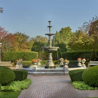 A tranquil garden scene featuring a central fountain surrounded by lush greenery and neatly trimmed hedges.