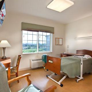 A hospital room with a bed, desk, and television.