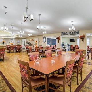 A spacious dining room with multiple tables and chairs arranged neatly, featuring warm lighting and a polished wood floor.