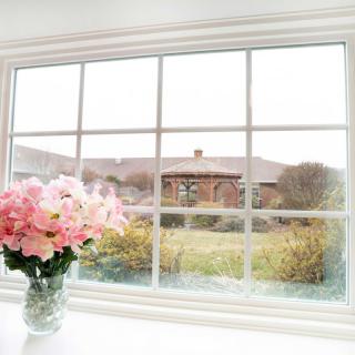 A vase of pink flowers sits on a windowsill, overlooking a garden and house outside.